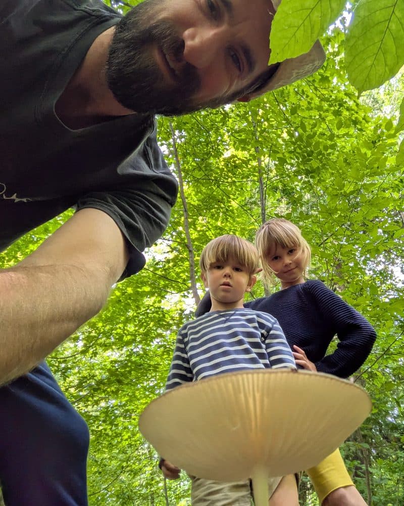 Michael with his kids in the woods, looking at a mushroom